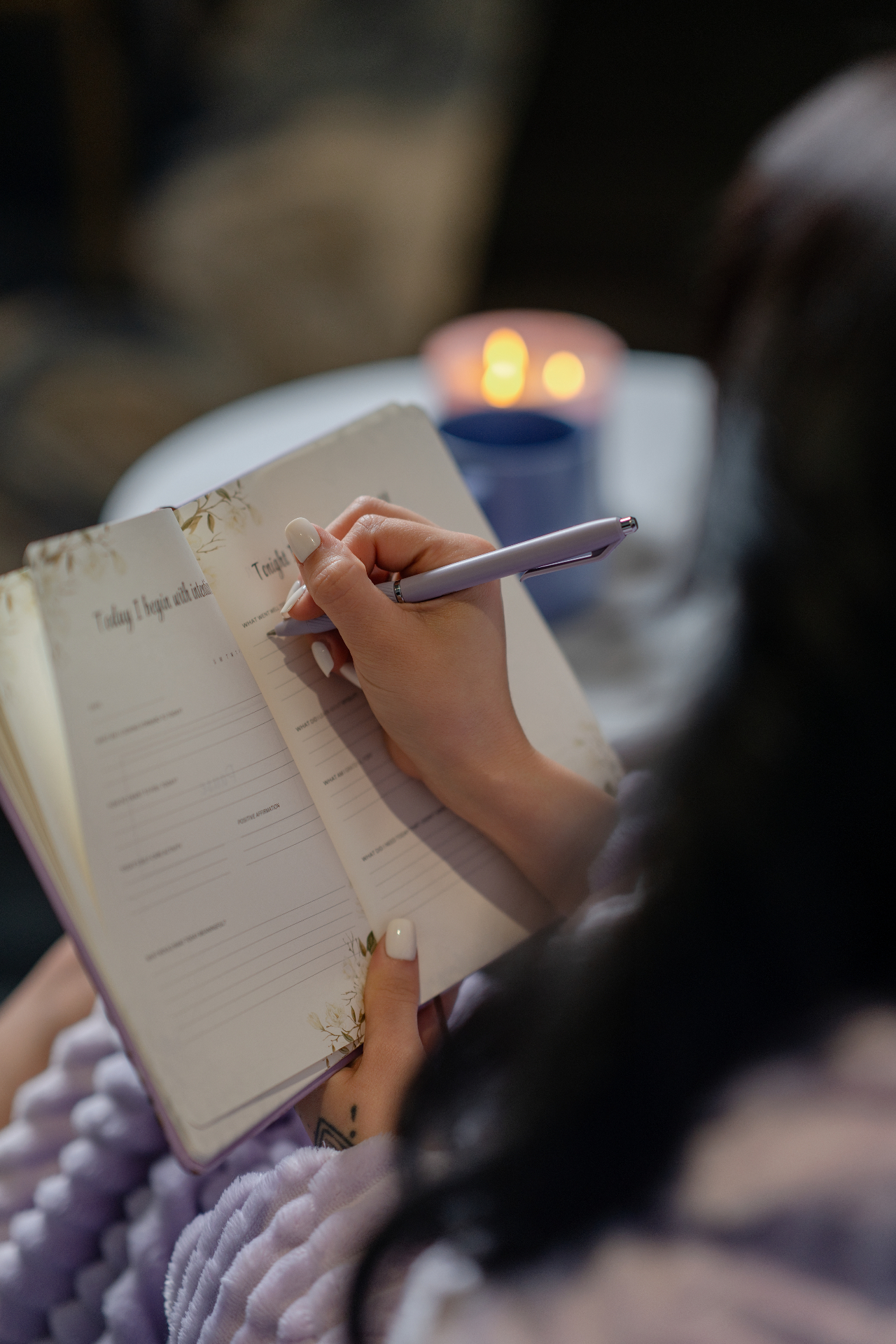 A woman writing in The Grace Journal with candles in the background
